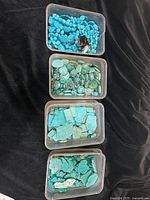 Four plastic containers filled with assorted turquoise beads, showing varied shapes and sizes