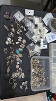Full spread of sterling silver findings on black cloth, plastic box of jump rings and sealed packs of earring backs