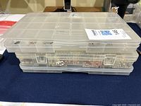 Three-layered plastic compartment organizer box with clear lid containing silver jewellery findings.