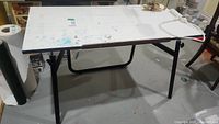 White rectangular table with black adjustable legs showing paint and use marks on surface.
