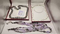 Overview of three necklaces displayed in open jewelry boxes, showing agate beads, freshwater pearls with green crystals, and mixed purple beads.