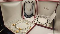 Three necklaces displayed in jewelry boxes: one with white beads and gold plated chain, one with rock crystals and onyx beads with sterling silver, and one with a sterling silver chain and dark crystals with rondelles.