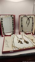 Three necklaces and pair of earrings displayed in boxes: black and gold bead necklace, black onyx and gold bead necklace on cord, mother of pearl and green bead necklace with sterling silver, and gold plated chain earrings with faceted black onyx