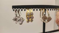 Three pairs of earrings on a display stand: large faceted crystals in sterling silver, gold plated hoops with crystal droplets, and silver hoops with crystal chips.