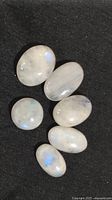 Six white cabochon cut opals arranged on black fabric, showing varying sizes and shapes under light.