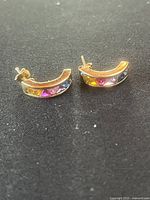 Pair of 10 karat gold curved earrings showing colored imitation stones on front face.