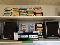 Wide view of the 8 track player, speakers and stacked 8 track tapes on shelves
