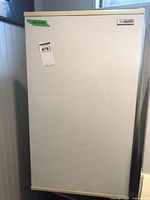 Closed front view of white Beaumark bar fridge, showing plain door with brand label at top right corner.