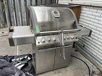 Front view of grill showing stainless steel hood, control panel and side shelf; cover visible on left.