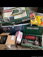 Lot overview showing green metal propane stove, blue cooler, yellow ropes, and a lantern