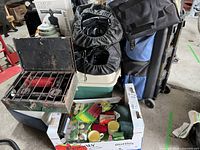 Wide view of the camping lot showing Coleman stove, camping pads, cooler, and assorted candles and accessories in box