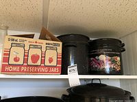 Shelf with boxed mason jars and multiple black speckled canning pots