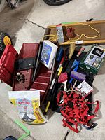 Wooden creeper with headrest, red metal ramps, tie-down straps, bag of Safe Step, assorted brushes, hand tools, and boxed accessories all arranged on a concrete floor.