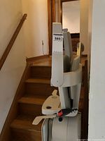 Side view of the chair lift mounted at the bottom of the wooden staircase, showing the seat and safety belt.