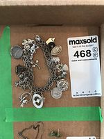 Charm bracelet laid flat with multiple charms including animal, coin, floral designs, and others visible, showing overall condition and metal type.