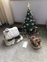 Full lot view showing three ceramic Christmas decorations on carpeted floor near a wall.