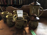 Photo displaying full coffee set: coffee pot, creamer, and four mugs with visible mushroom finials and mushroom designs on ceramic surfaces.
