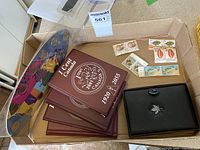 Five burgundy 1 Cent Canada coin books with years 1920 to 2055, a black leather like case with a maple leaf embossing, and some stamps in background.