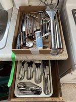 Cutlery pieces including spoons, forks, knives neatly placed in drawer organizer and kitchen utensils in box above.