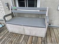 Front view of gray resin deck storage bench with hinged lid for storage compartment and attached backrest.