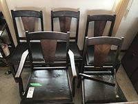 Overview of all five chairs showing one armchair and four straight-backed chairs with leather seats and wood design on backs.