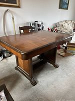 Full view of wooden dining table set up with leaf inserted, showing rectangular shape and base structure.