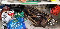 Image showing the lot area including gardening tools and accessories around the folding table, none included in sale.