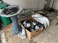 Resin bird bath with soil residue and surrounding items including small lighthouse ornament and box of solar garden lights.