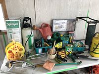 Full view showing the Mastercraft lawn and garden sprayer in box, white hand sprayer, red watering can, hose reel, green bin with hand tools, wooden basket with clothespins, and fertilizer bottles.