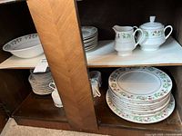 Photo of wooden cabinet shelves with stacked Gibsons Christmas-themed china including plates and serving pieces