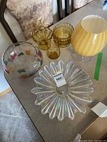 Glassware collection on a table including amber colored glass bowls, clear glass with colored square accents, iridescent wavy bowl, and yellow footed glass piece.