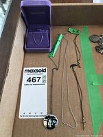 Two pendants photographed in a cardboard box, one in a purple velvet Ben Moss case and the other on a chain with a round design pendant.