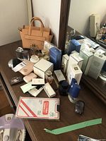 Full lot overview showing tan handbag and multiple perfume bottles and boxes on wooden surface in front of mirror.