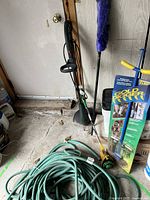 Yardworx electric grass trimmer, green garden hose, Blue duster brush, Gold Digger garden tool box and other garden tools grouped near door
