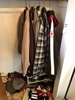 Men's jackets and sweaters hanging on a closet rack with hats and scarves arranged below