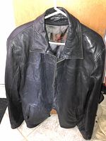 Front view of a men's black Danier leather jacket with a collar and dual front pockets, hanging on a hanger.