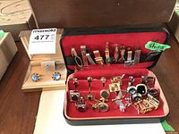 Photo showing a collection of men's cuff links and tie pins in a red velvet-lined case and a smaller box containing blue stone cuff links.