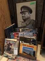 Framed black and white photo of a military officer wearing a peaked hat and trench coat, surrounded by various military books in front.