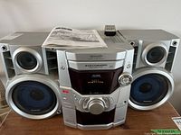 Front view of Panasonic mini stereo system with two speakers, 5-disc CD changer and central control knob, remote control and manual placed on top