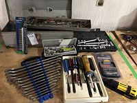 Tools laid out including wrenches, screwdrivers, ratchets, socket set pieces and a toolbox on a wooden surface