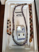 Photo showing two necklaces and a card with auction lot number labeling them as including jewelry made from Quahaug shell.