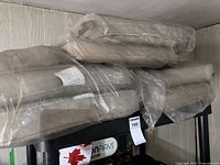 Multiple beige outdoor chair cushions stacked and partially wrapped in plastic on a black shelving unit.