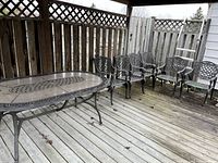 Wide view of oval table and six matching chairs arranged on wooden deck under lattice fence