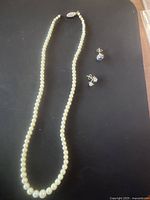 Photo showing cultured pearl necklace with decorative clasp, single Tanzanite diamond stud earring, and pair of sterling silver earrings.