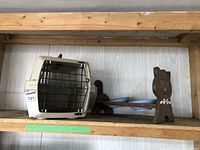 Shelf view of pet carrier next to wooden feeding station with two blue bowls.