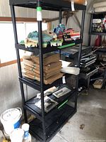 Black plastic shelving unit with multiple levels containing vintage toy boats and cardboard stacks.
