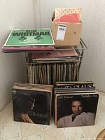 Photo showing the metal stand filled with a large collection of vinyl record albums and some albums stacked on top, along with a cardboard box on the upper shelf containing more records.