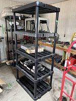 Full view of the black resin 5-tier shelving unit assembled in a garage or workshop setting, showing shelving details and overall condition.