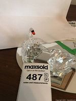 Two Swarovski crystal swan figurines on a mirrored surface; one with wings extended and one resting.