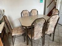 Kitchen table with six matching chairs with black chrome frames and patterned upholstery arranged around it in a tiled kitchen floor setting.